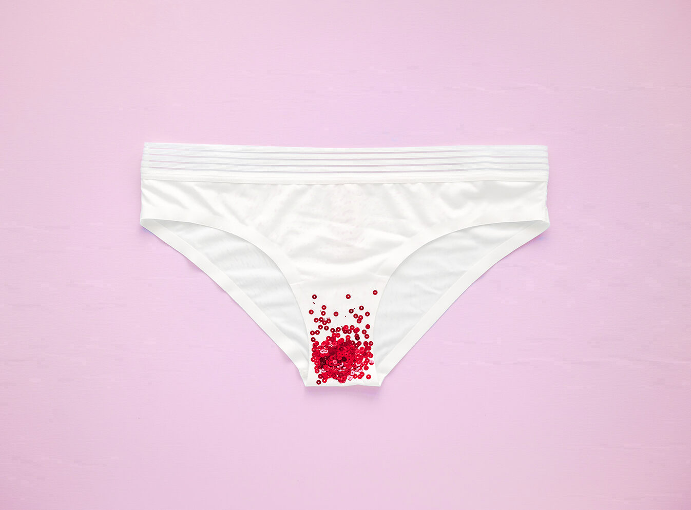 A pair of white panties with red sequins at the bottom in front of a pink background